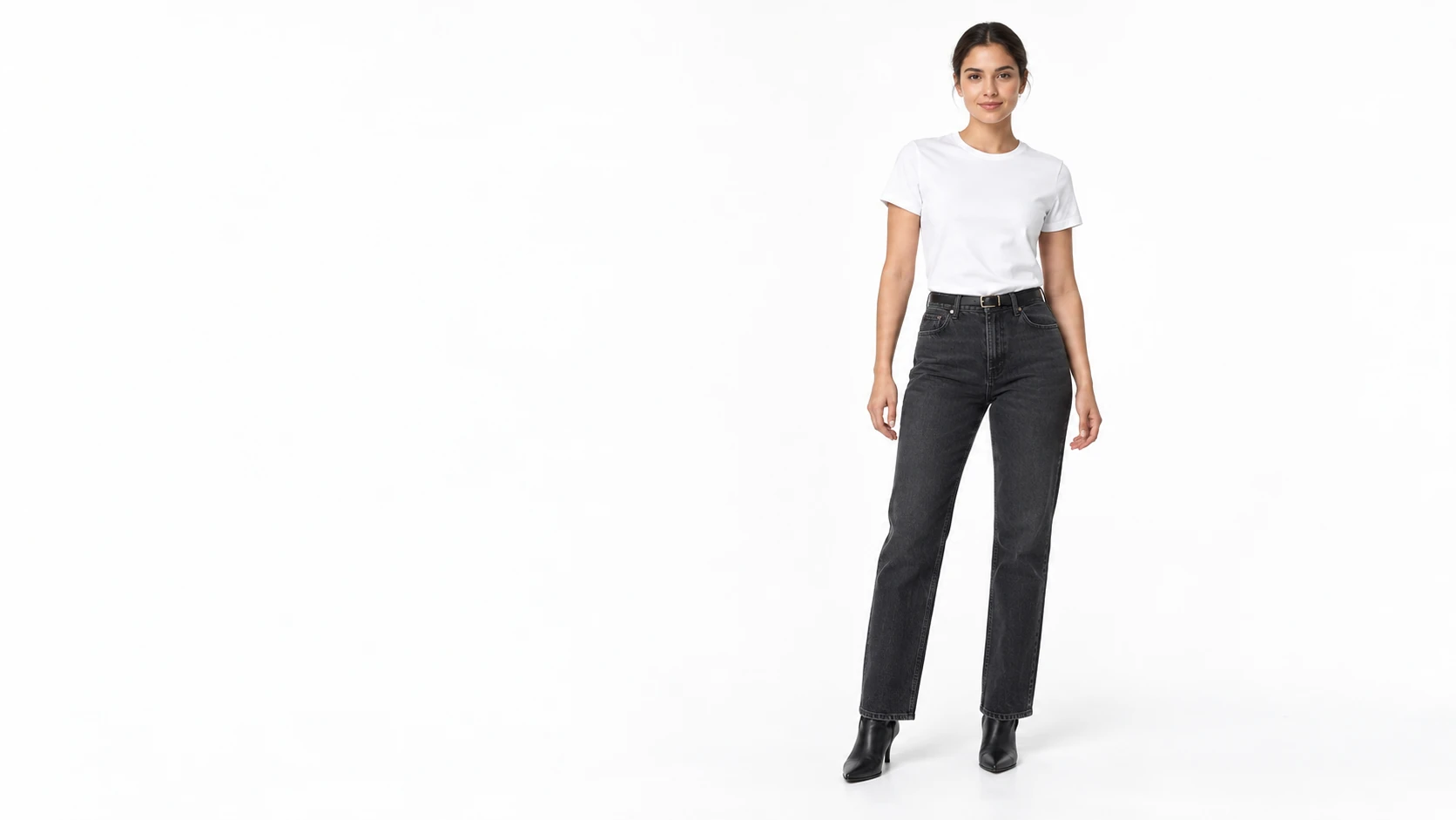A woman wearing a white T-shirt, charcoal jeans and black ankle boots in a white studio